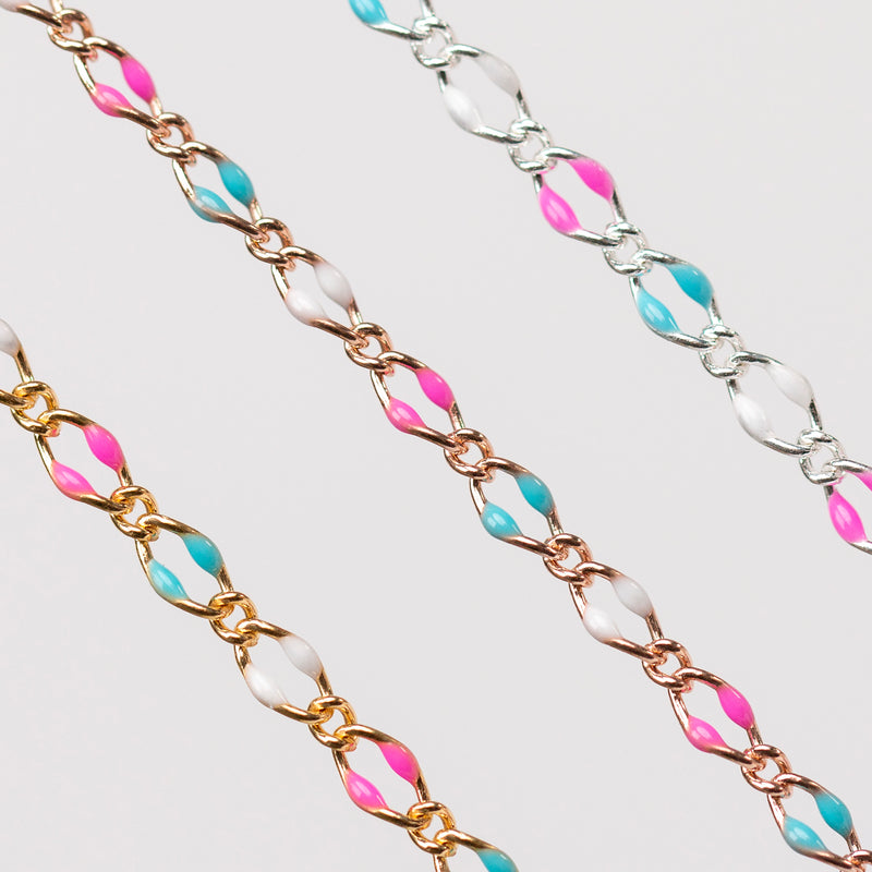 Up close of three chains with links that are gold, rose gold, and silver. Enamel beads in pink, blue, and white are shown.