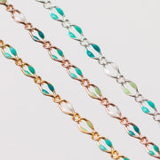 Up close chain with green, teal, blue, and white enamel beads. Three chains with gold, rose gold, and silver on plain background.