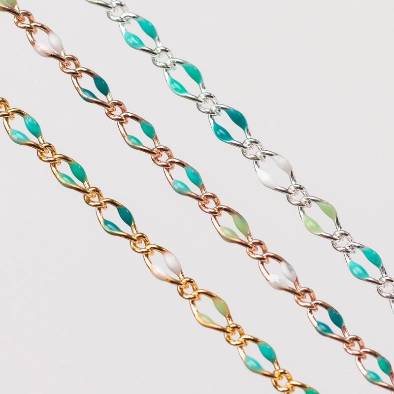 Up close chain with green, teal, blue, and white enamel beads. Three chains with gold, rose gold, and silver on plain background.