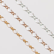 Zoomed in photo of three chains with white enamel on a gray background. One chain is gold, one is rose gold, and one is silver.