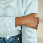 A hammered textured gold filled yellow gold chain on a models wrist. Model is resting hand on other arm.