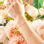 Rose colored gold filled chian with textured oval links on models hand. Models hand is in front of flowers.
