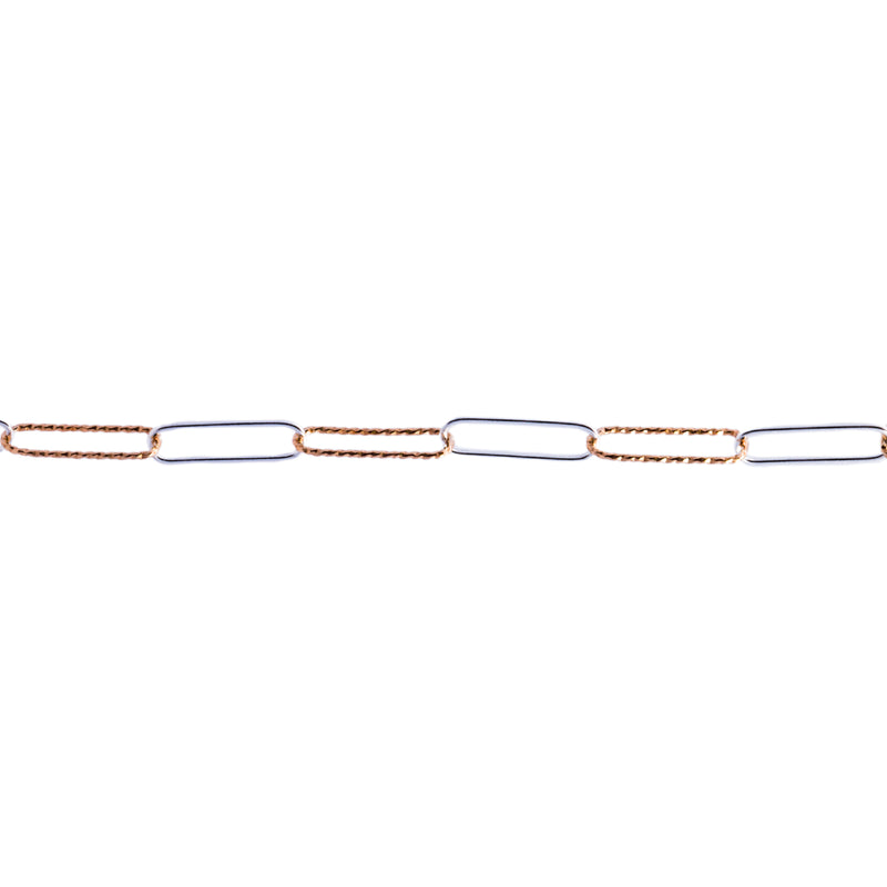 A close-up of a mixed metal chain featuring alternating elongated links, with one side in textured yellow gold and the other side in smooth silver metal, set against a plain white background.