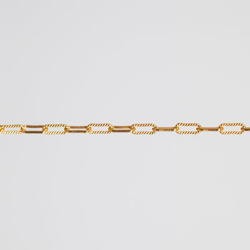 A close-up of a gold chain featuring alternating smooth oval links and twisted rope-style oval links, set against a solid light gray background.