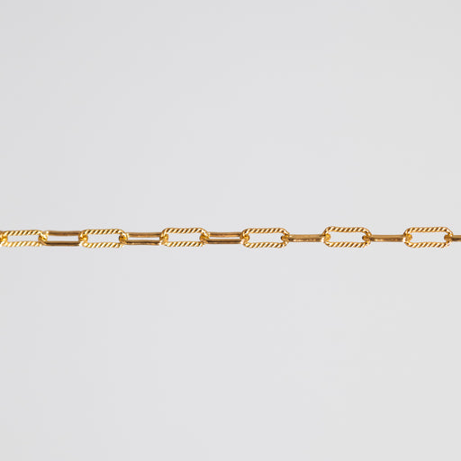 A close-up of a gold chain featuring alternating smooth oval links and twisted rope-style oval links, set against a solid light gray background.