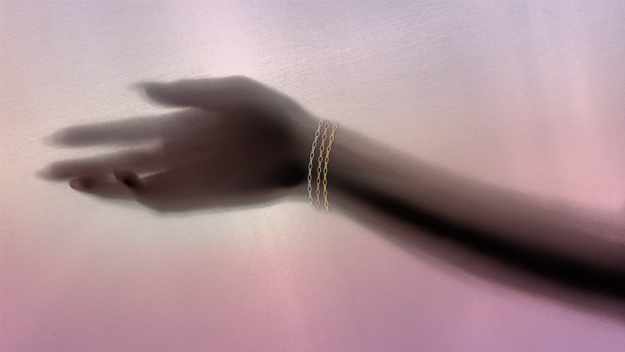 A hand behind a pink sheet casting a shadow. The shadow is wearing all three colored versions of the pj chain.