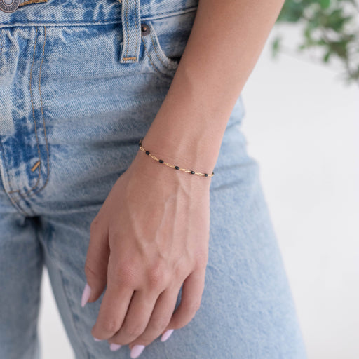 Woman wearing a gold chain on her wrist that has black enamel on it