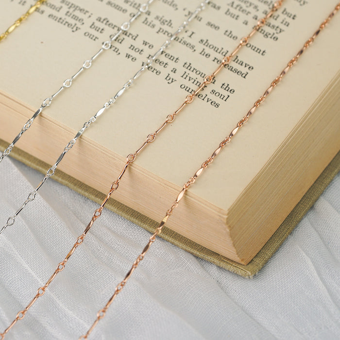 Permanent jewelry chain laid out on top of a book to showcase it's design and colors.