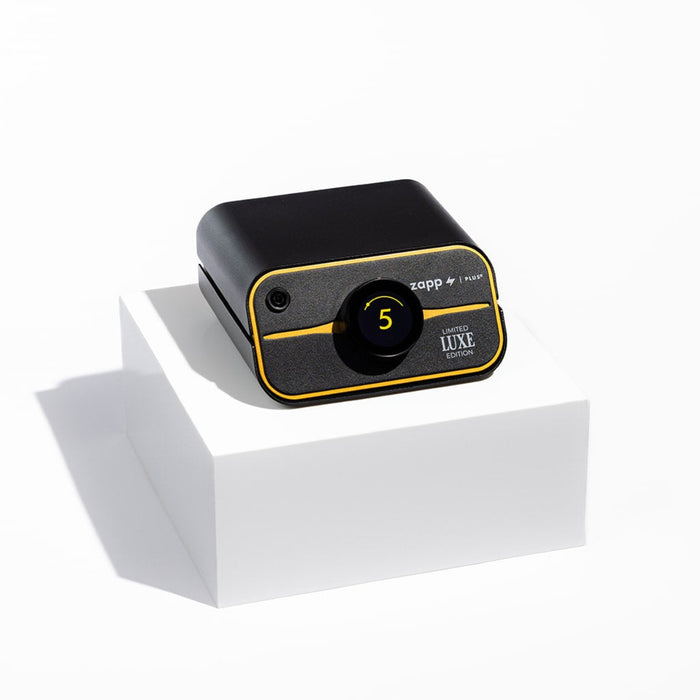 Black and gold Zapp Plus permanent jewelry welder on a square white pedestal casting a shadow on a white background