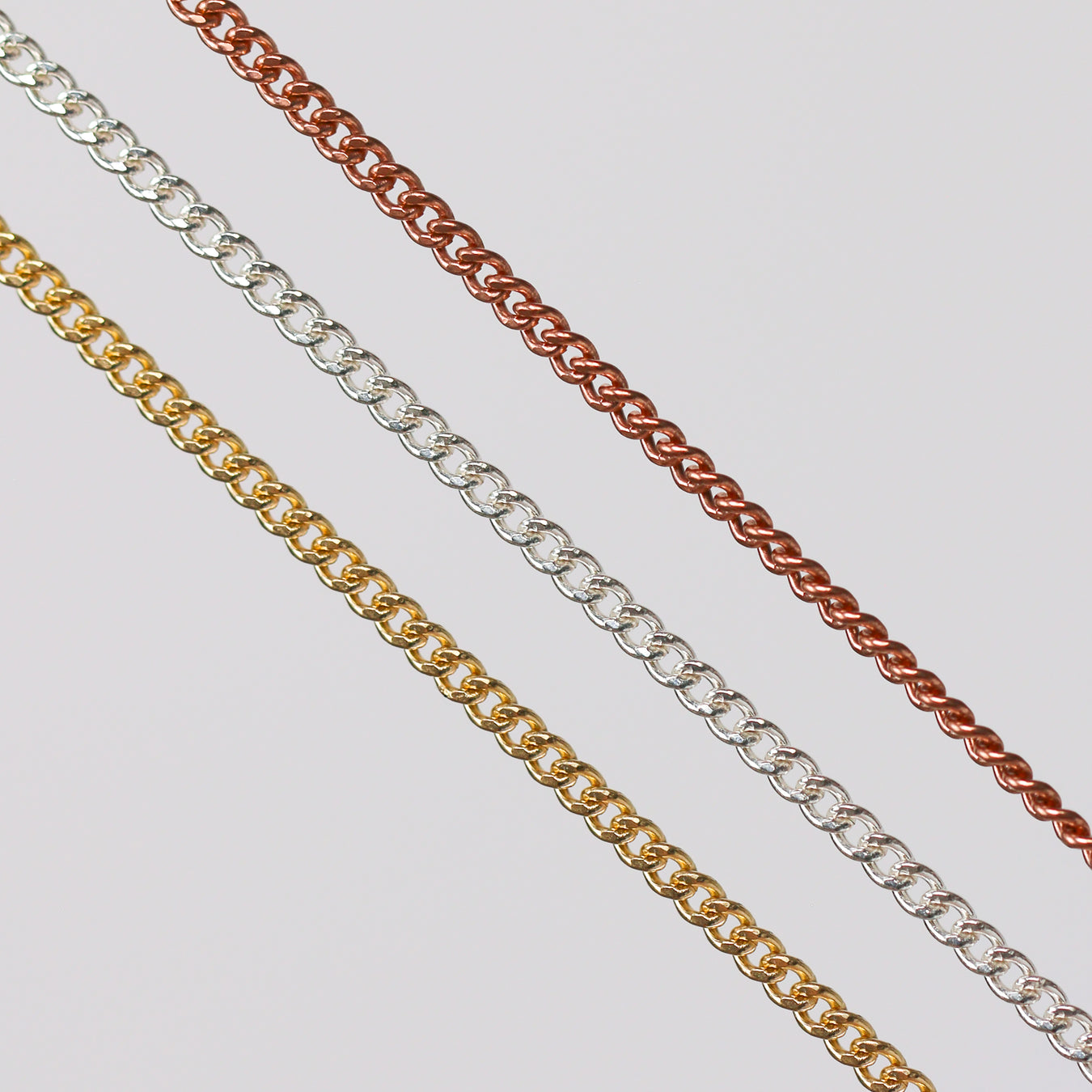 Three pj chains laying side by side in different metal types over a gray background
