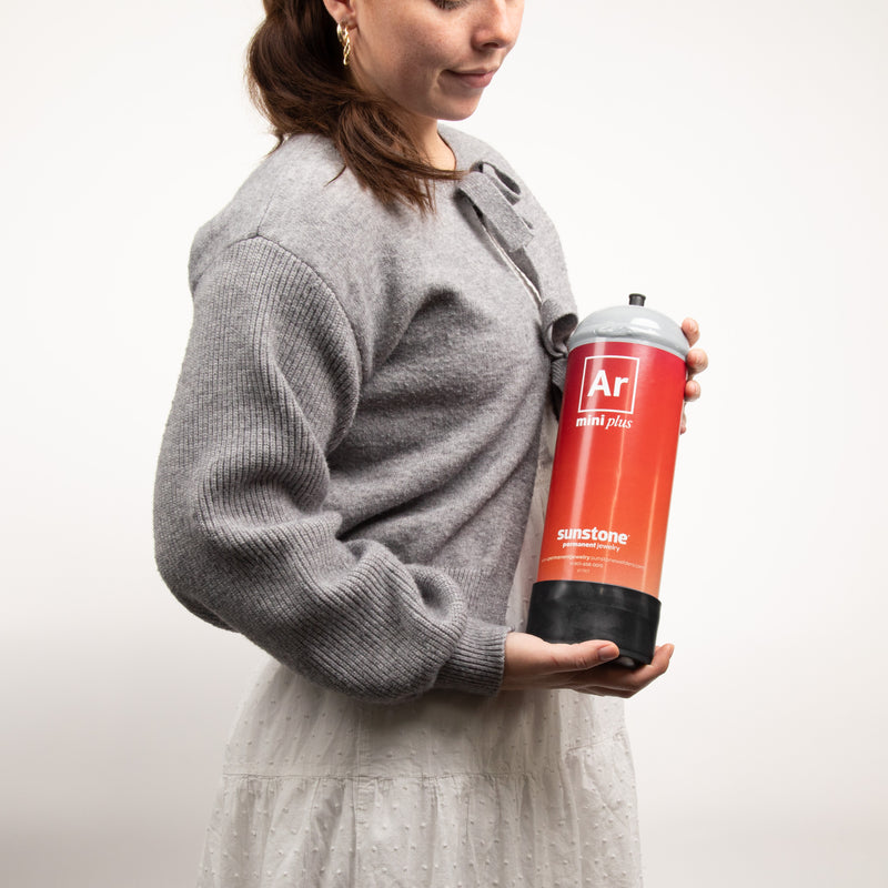 Woman holding a red and black gas canister with sunstone permanent jewelry branding against a white background