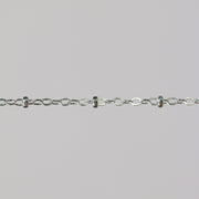 Close-up of a silver chain with beads on a light gray background