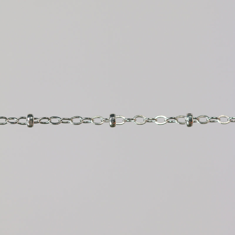 Close-up of a silver chain with beads on a light gray background