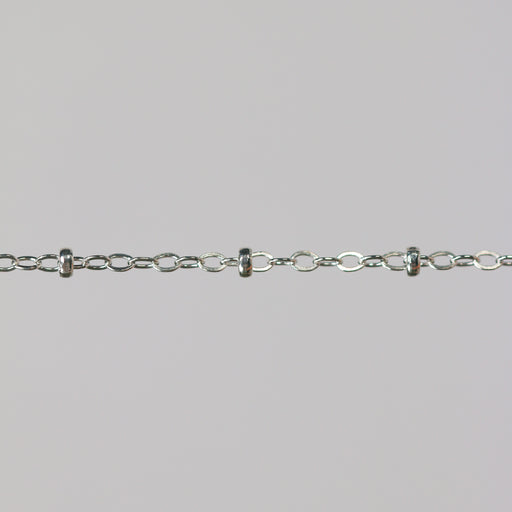 Close-up of a silver chain with beads on a light gray background