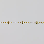 Gold chain with small cylinder beads on a light gray background