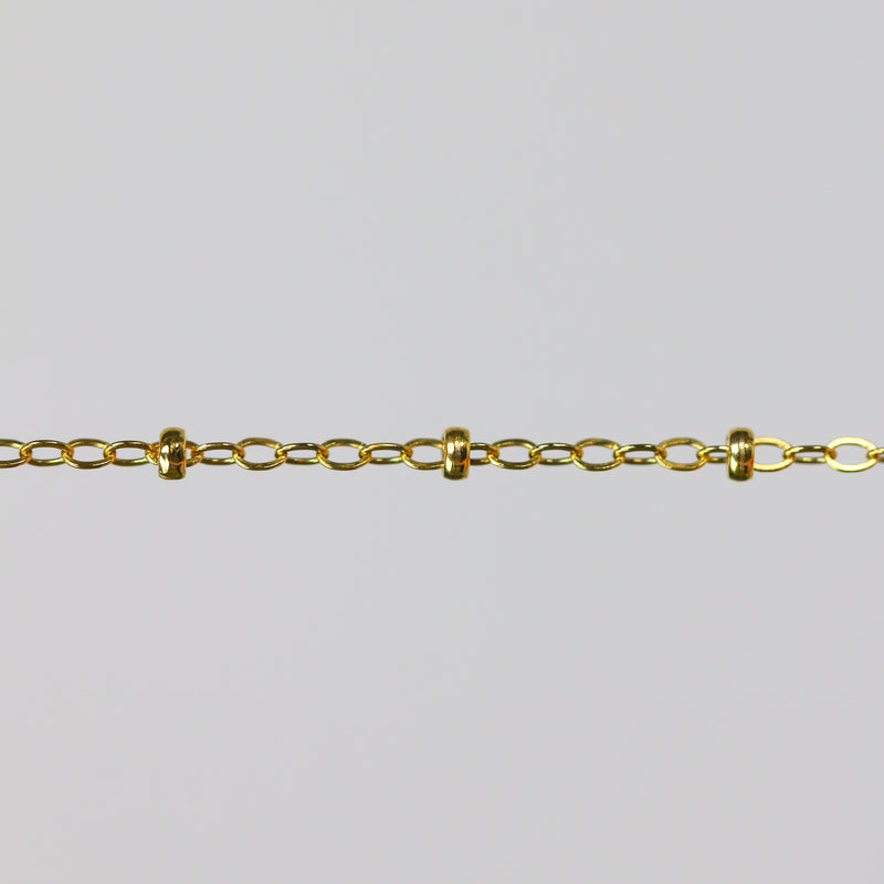 Gold chain with small cylinder beads on a light gray background