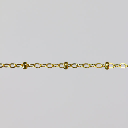Gold chain with small cylinder beads on a light gray background