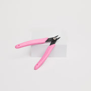 Pink pliers leaning on a white box against a white background