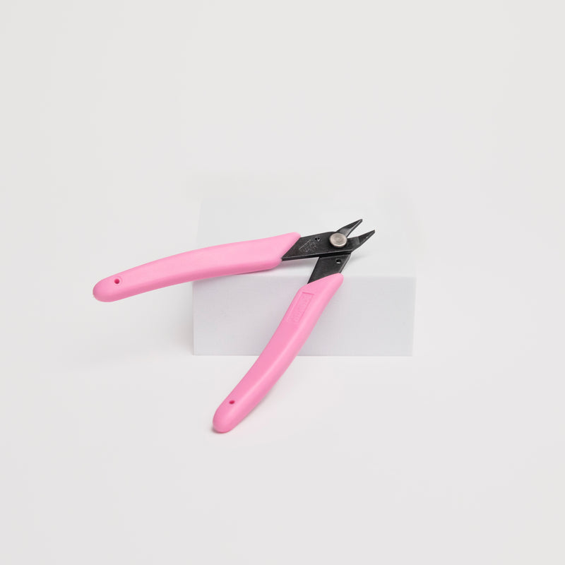 Pink pliers leaning on a white box against a white background