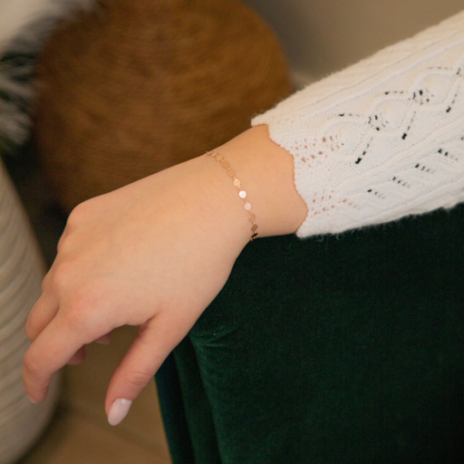 Close-up of a hand wearing a gold continuous disk bracelet with a blurred background