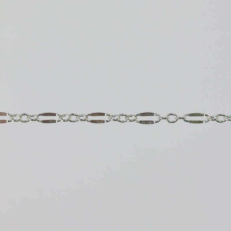 Closeup of a silver chain that has elongated links that are dapped and regular round links.