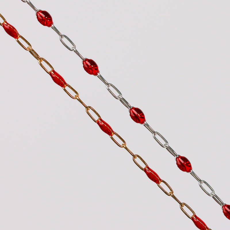 Gold and silver chains with red enamel beads on them over a gray background