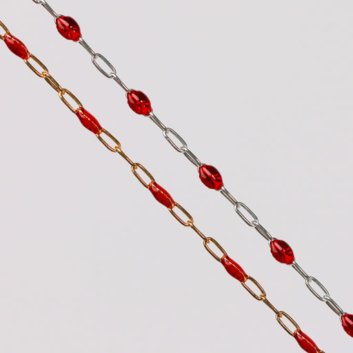 Gold and silver chains with red enamel beads on them over a gray background