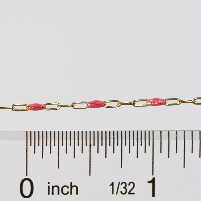 Gold chain with pink enamel next to a ruler for measurement on a white background