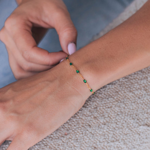 Woman wearing a gold cable chain bracelet with green enamel beads on a textured surface