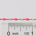 Gold chain with pink rose enamel next to a ruler for measurement on a white background