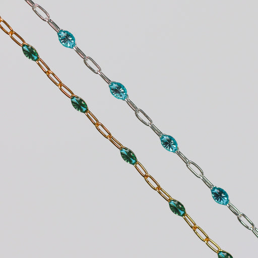 Two chains with teal enamel on them. One gold and one silver one side by side on a light gray background