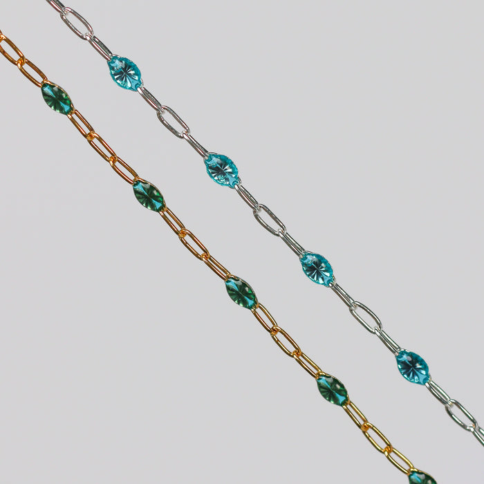 Two chains with teal enamel on them. One gold and one silver one side by side on a light gray background