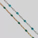Two chains with teal enamel on them. One gold and one silver one side by side on a light gray background