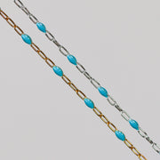 A yellow gold and a sterling silver chain with turquoise light blue enamel over a gray background