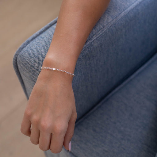 Person wearing a silver rolo chain bracelet on a blue couch