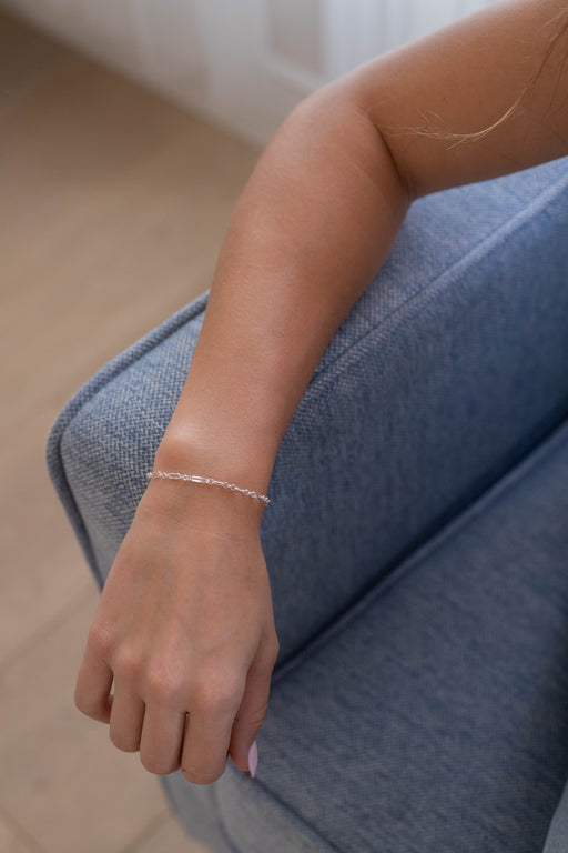 Person wearing a silver rolo chain bracelet on a blue couch