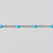 Silver bracelet chain with turquoise enamel on it over a gray background