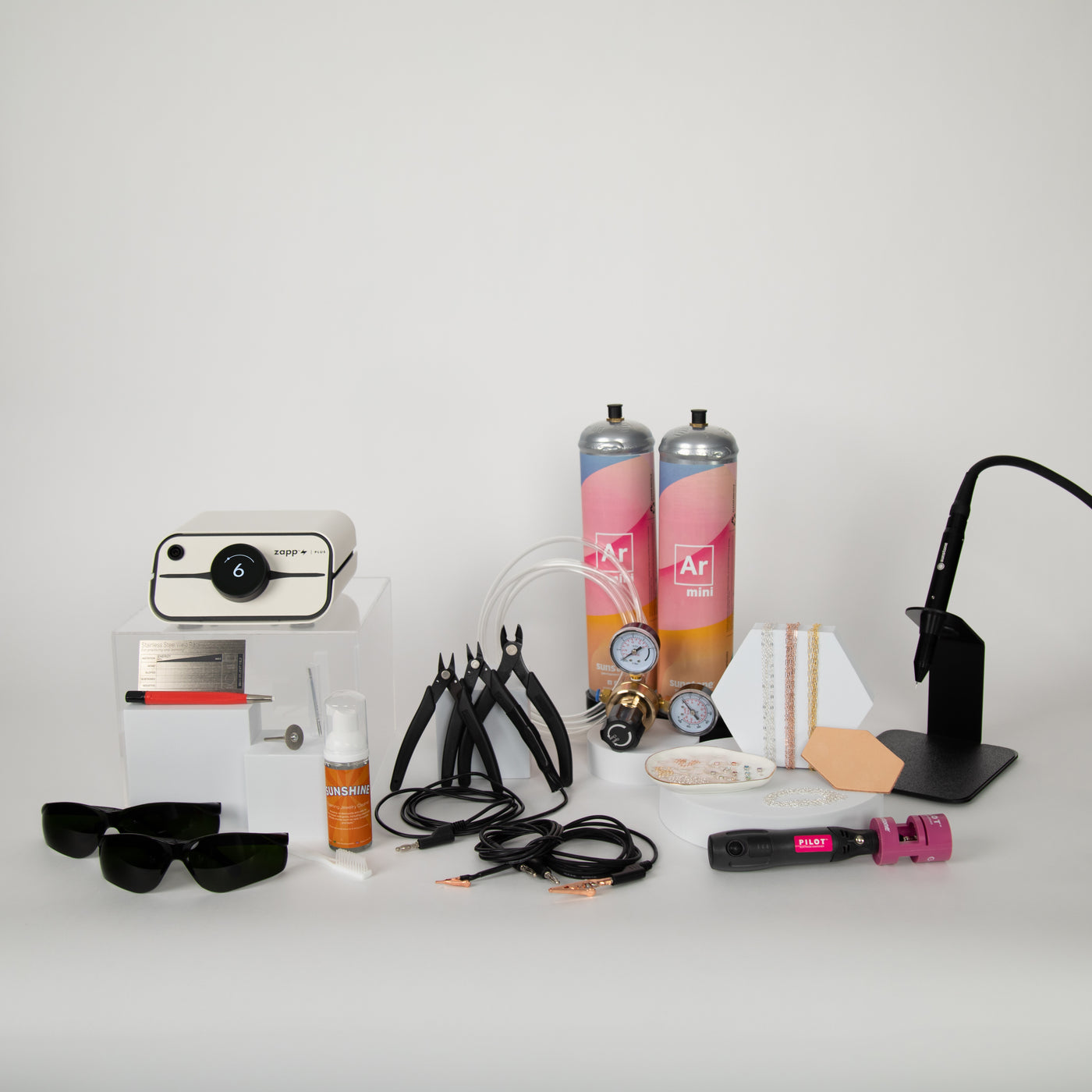 Collection of various items including a pj welder, argon gas, tools, accessories, and permanent jewelry supplies on a white surface with a white background