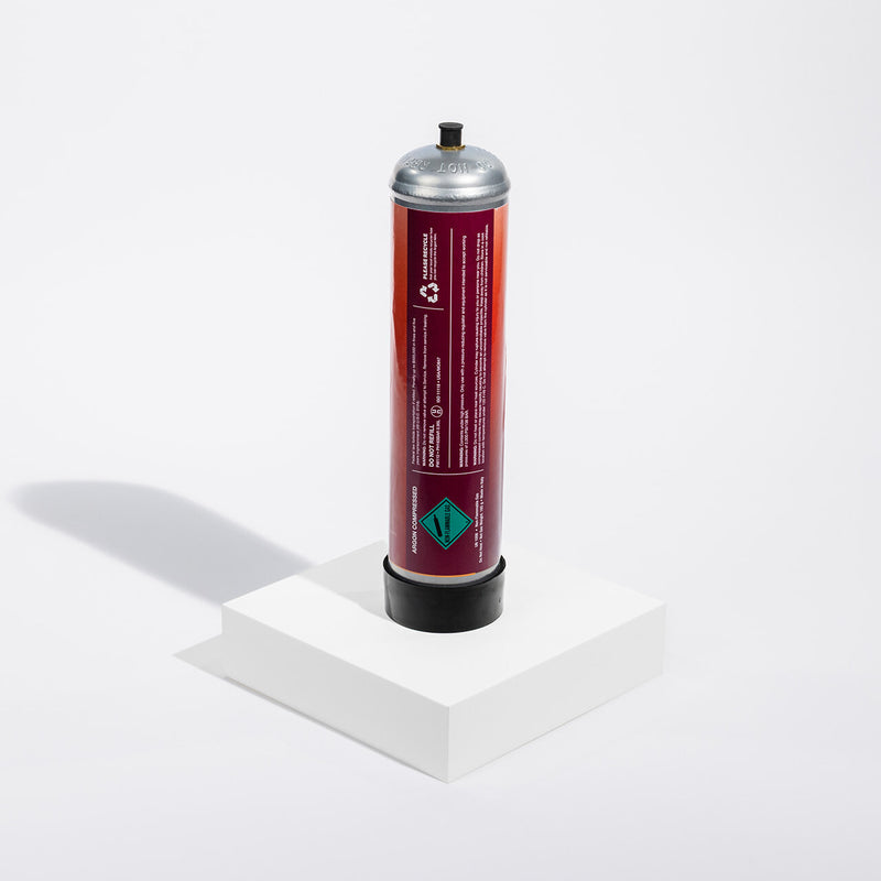 Cylindrical argon gas container with a red label on a white background standing on a white platform with a gray colored shadow