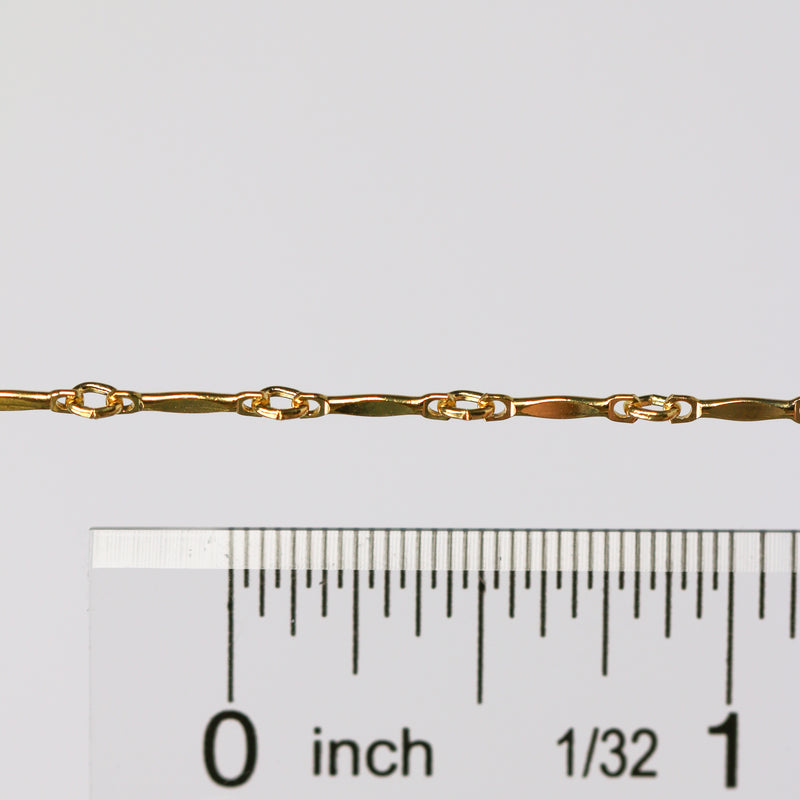 The Brittany chain in gold shown up close next to a ruler showcasing the size of the links and dapped bar design.