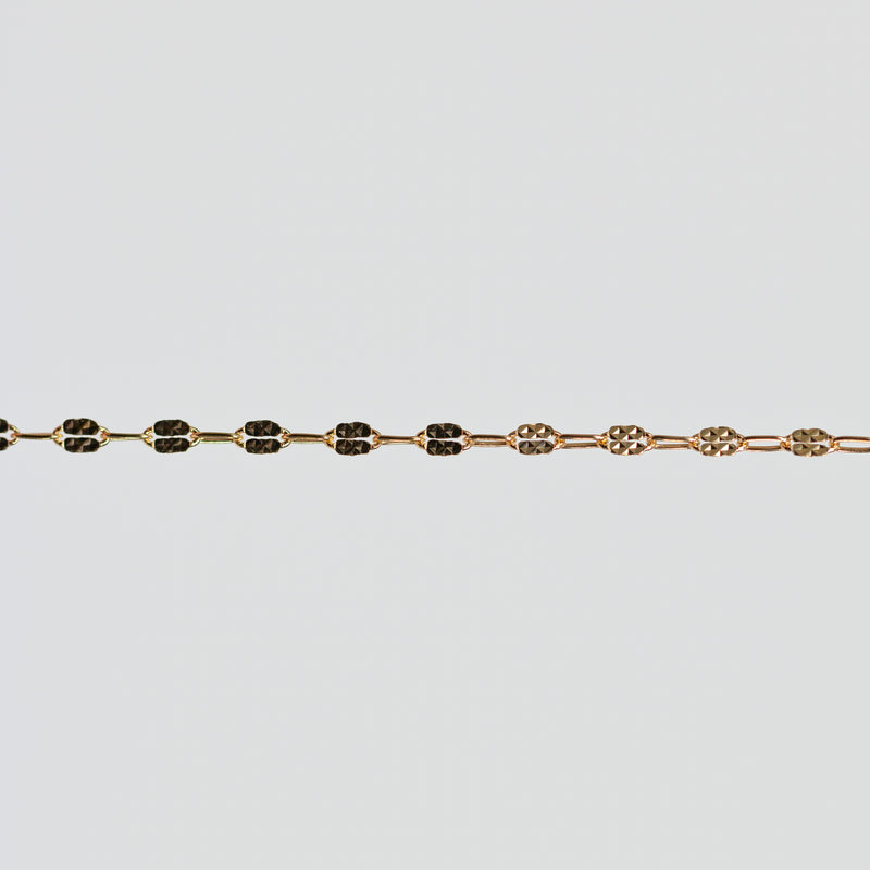 Gold bracelet with hammered squares on the links over a light gray background
