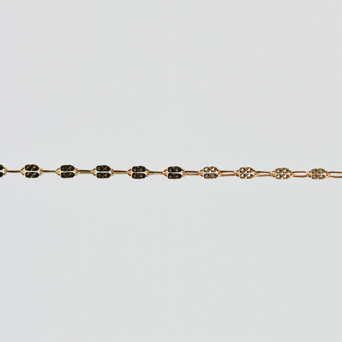 Gold bracelet with hammered squares on the links over a light gray background