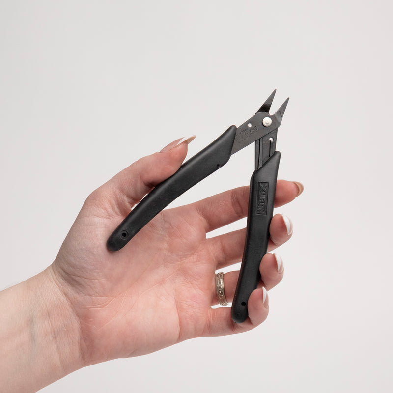 Hand holding a pair of black pliers on a light gray background