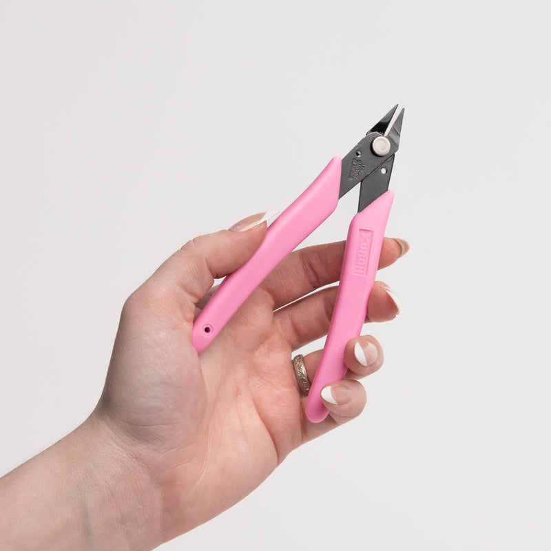 Hand holding pink permanent jewelry pliers against a light gray background