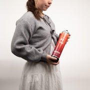 Person holding a mini tank of argon gas with a sunstone logo and argon gas symbol on a plain background