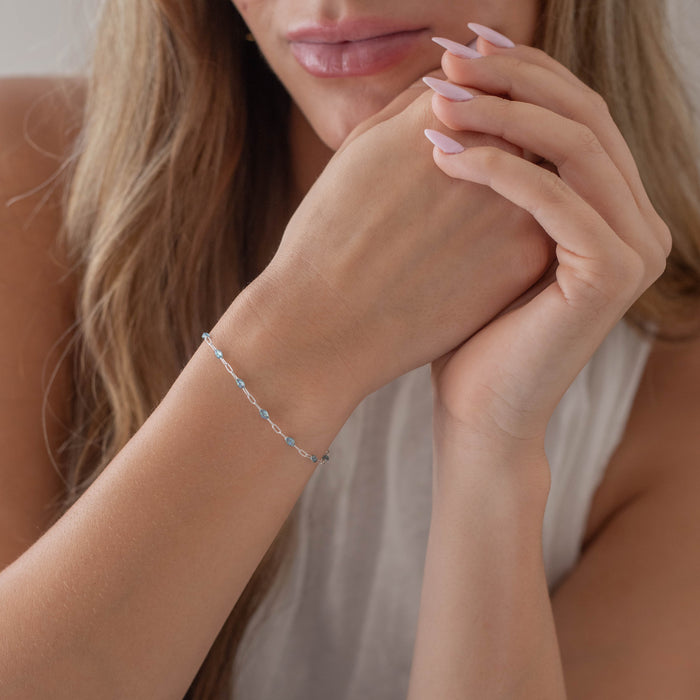 Close up of a woman's hand with an opal enamel permanent jewelry chain on it.