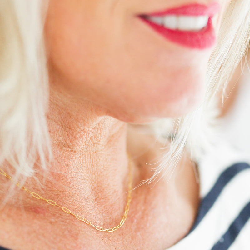 Close-up of a person wearing a gold paperclip chain necklace with a blurred background