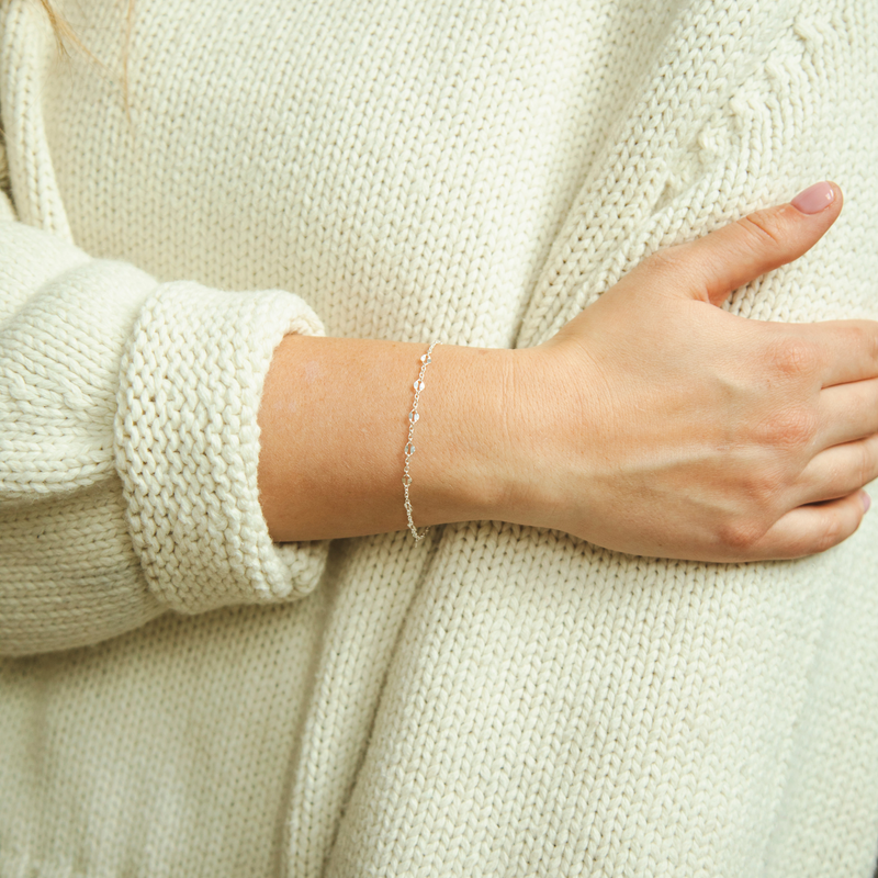 Woman wearing a delicate bracelet chain on her wrist while holding the sleeve of her sweater on her other arm