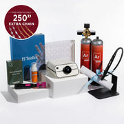 A jewelry making kit displayed on white pedestals against a clean white background, including a cream-colored heat press machine, two orange argon gas cylinders labeled 'Ar mini', a blue PJ Toolkit box, a small orange jewelry cleaner bottle, a black chain tool, a pink and black electrode sharpener, and a white rolled sheet tied with a light blue ribbon. A red circular badge in the top left reads 'THIS MONTH ONLY 250" EXTRA CHAIN'.