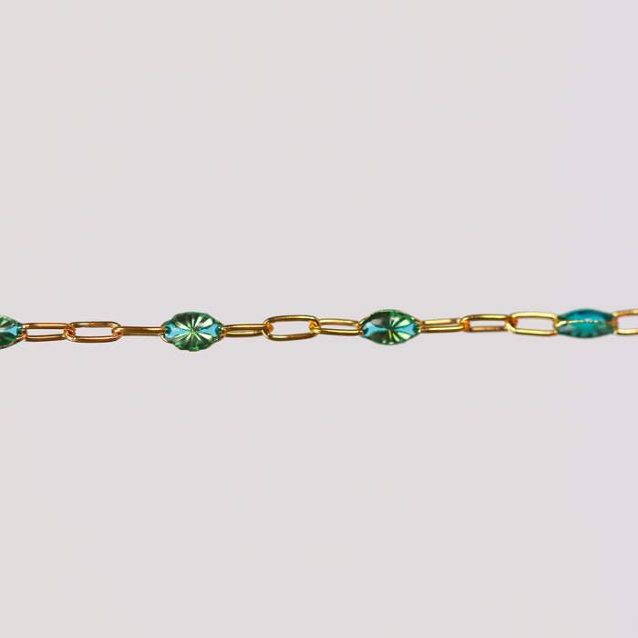 Gold chain bracelet with teal green blue enamel on it over a light gray background